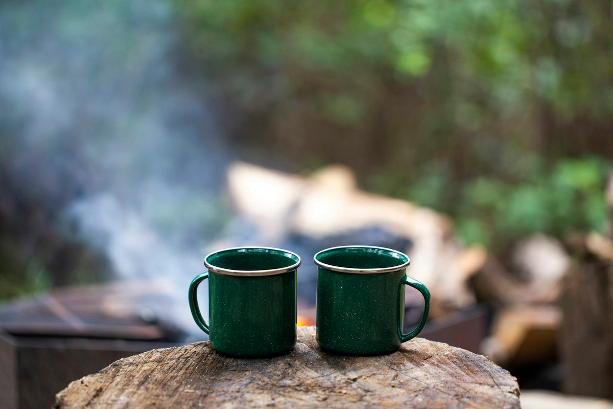 Two enamel mugs of coffee beside a smoky campfire